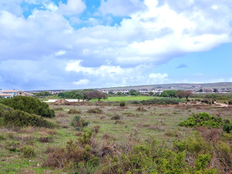 A scenic landscape view overlooking a golf course and surrounding residential estate under a cloudy sky.