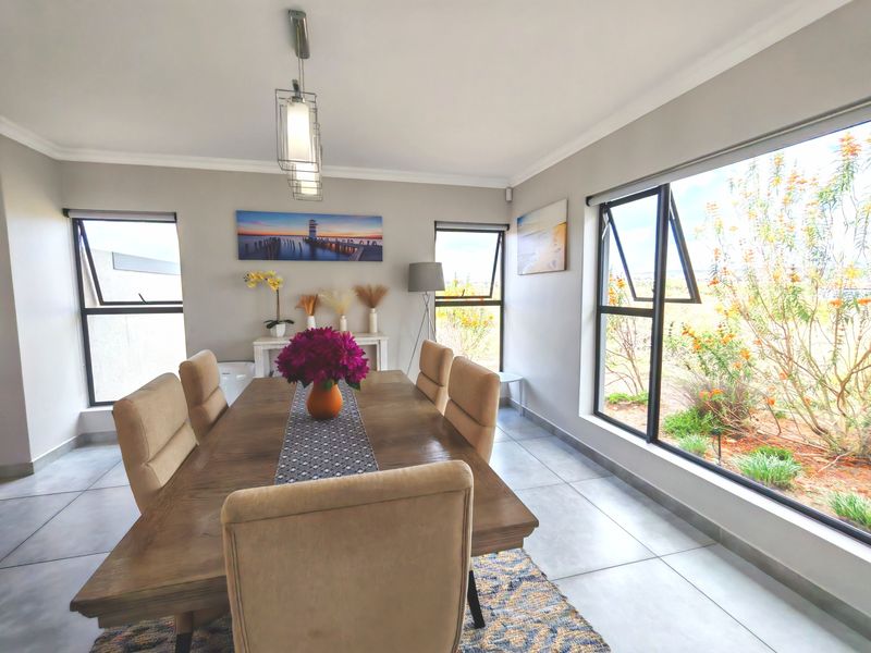 Bright dining room featuring large aluminium windows, neutral tiled flooring, and modern pendant lighting, offering a clean and well-maintained space for family meals.