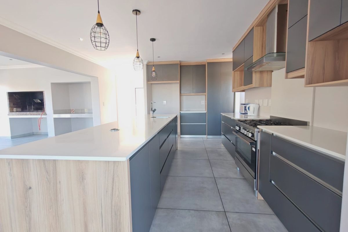 Modern kitchen featuring a large island with quartz countertops, sleek grey and wood-tone cabinetry, gas stove, and an adjacent built-in braai area.