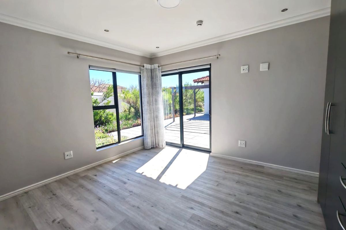 A bright, empty bedroom featuring modern laminate flooring, built-in cupboards, and sliding glass doors that open onto an outdoor patio area.