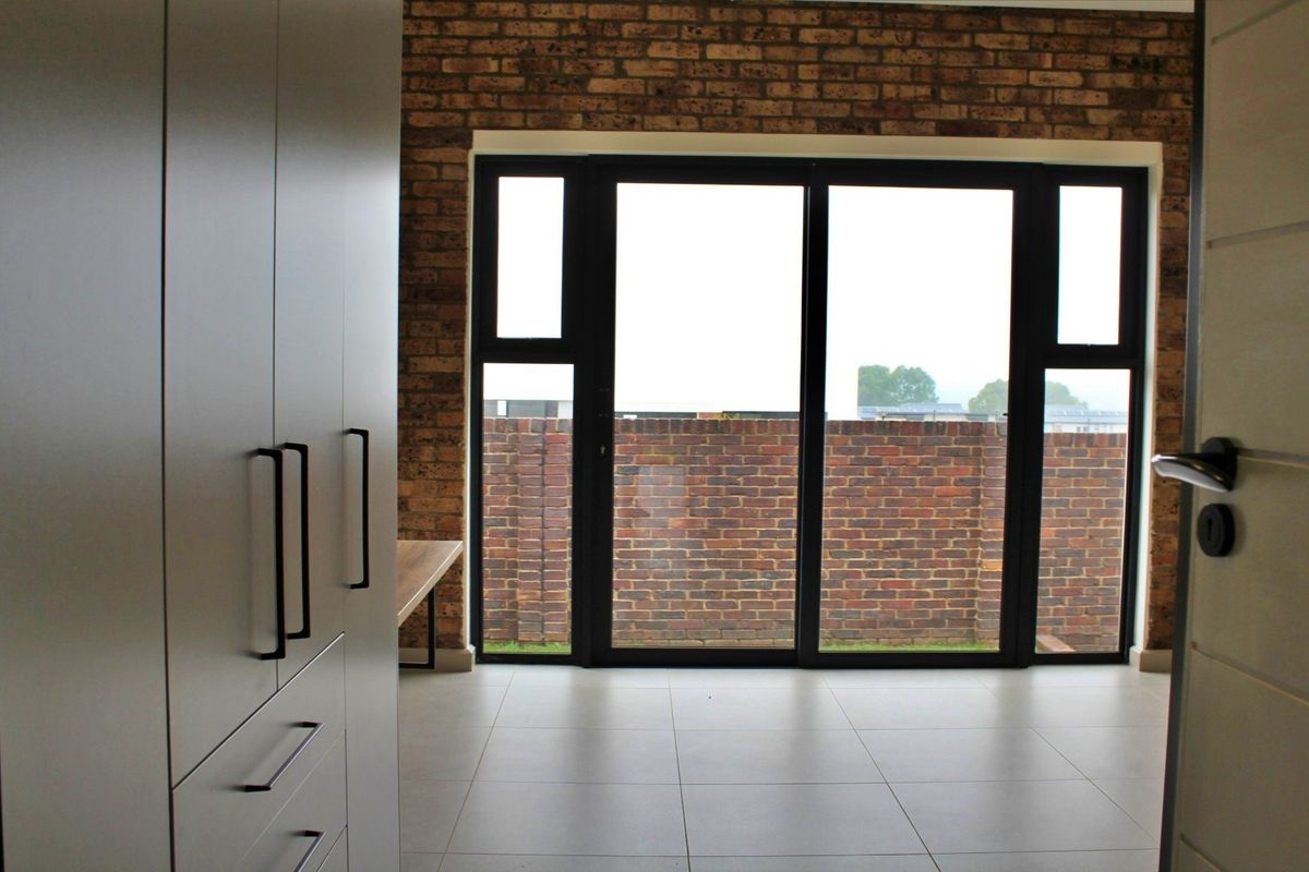 Modern bedroom featuring sleek built-in cupboards, an exposed brick feature wall, and large sliding glass doors leading to the exterior.