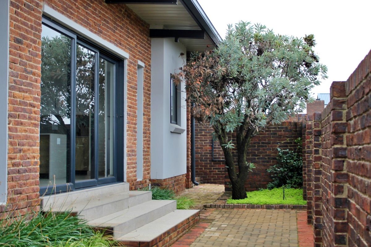 A well-maintained rear exterior featuring a brick facade, sliding glass doors, concrete steps, and a paved courtyard area with a boundary wall.