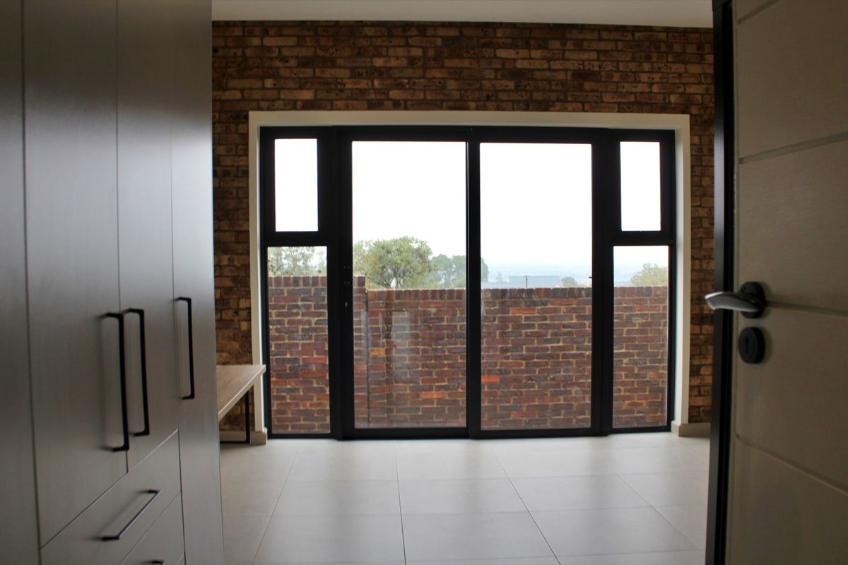 Modern bedroom featuring an exposed brick feature wall, sleek built-in cupboards, large sliding glass doors, and neutral tiled flooring.
