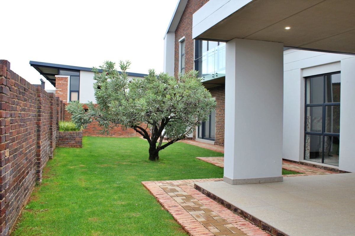 A well-maintained rear garden featuring a brick boundary wall, a paved walkway, and a covered patio area with modern architectural finishes.