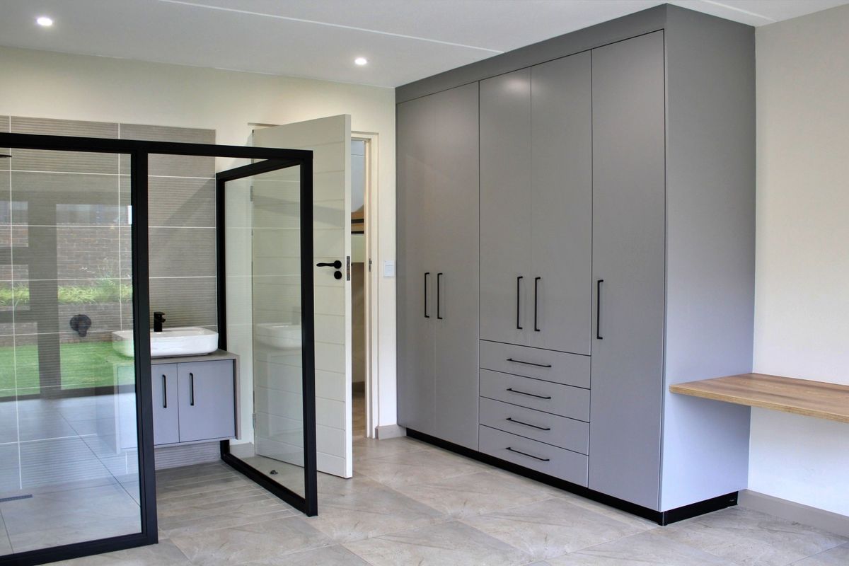 Modern bedroom featuring extensive built-in cabinetry, a floating desk, and an open-plan en-suite bathroom with a glass-enclosed walk-in shower.