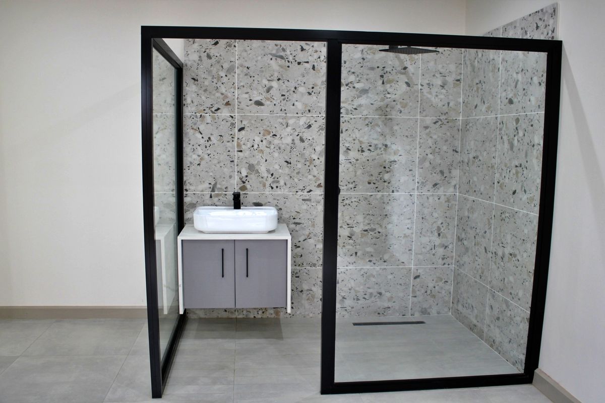 Modern bathroom featuring a walk-in shower with black-framed glass enclosure, terrazzo-style tiling, and a contemporary wall-mounted vanity with a vessel sink.