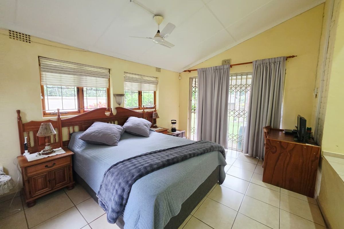 A bedroom featuring tiled flooring, a ceiling fan, and direct access to the garden through a sliding glass door with a security gate.
