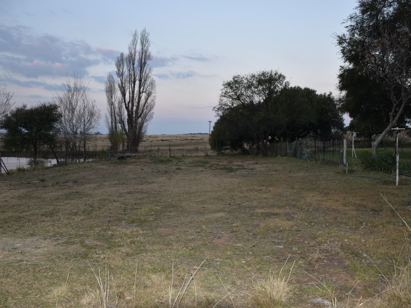 Expansive open garden area featuring mature trees and wire perimeter fencing, overlooking the surrounding rural landscape.