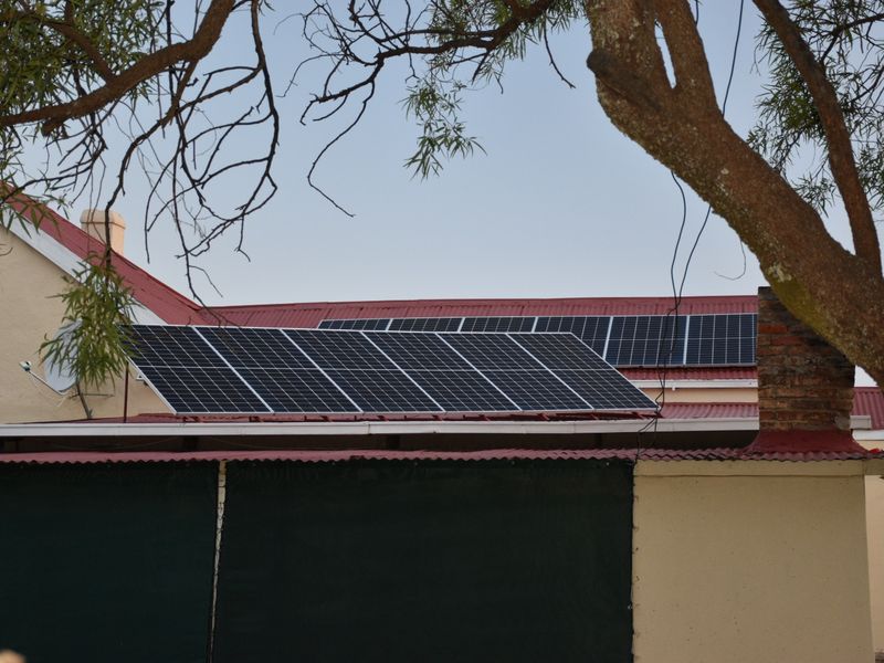 Rear view of the property featuring a corrugated metal roof equipped with a modern solar panel array and a brick chimney.