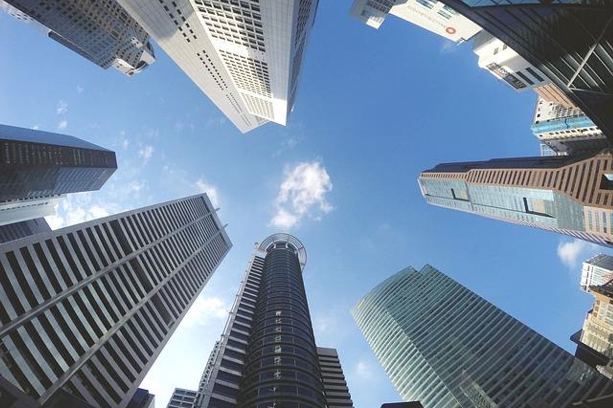 A low-angle perspective looking up at a cluster of modern high-rise commercial skyscrapers against a clear blue sky.