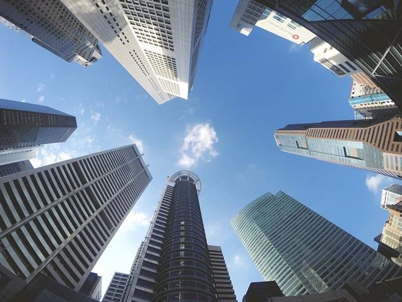A low-angle perspective looking up at a cluster of modern high-rise commercial skyscrapers against a clear blue sky.