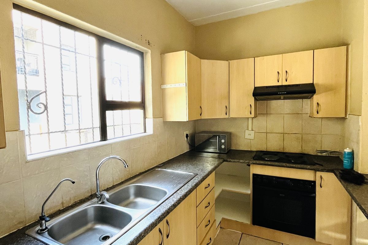 A functional kitchen featuring laminate cabinetry, built-in oven with hob, extractor fan, and a double basin stainless steel sink with tiled splashback.