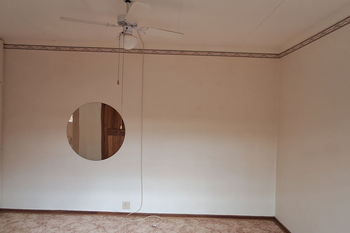 An empty bedroom featuring built-in cupboards, a ceiling fan, and carpeted flooring, ready for renovation or staging.
