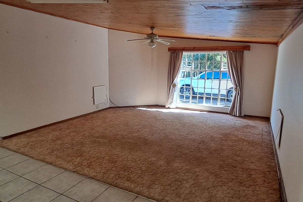 Spacious living area featuring a timber ceiling, ceiling fan, and a mix of tiled and carpeted flooring with a wall-mounted heater.