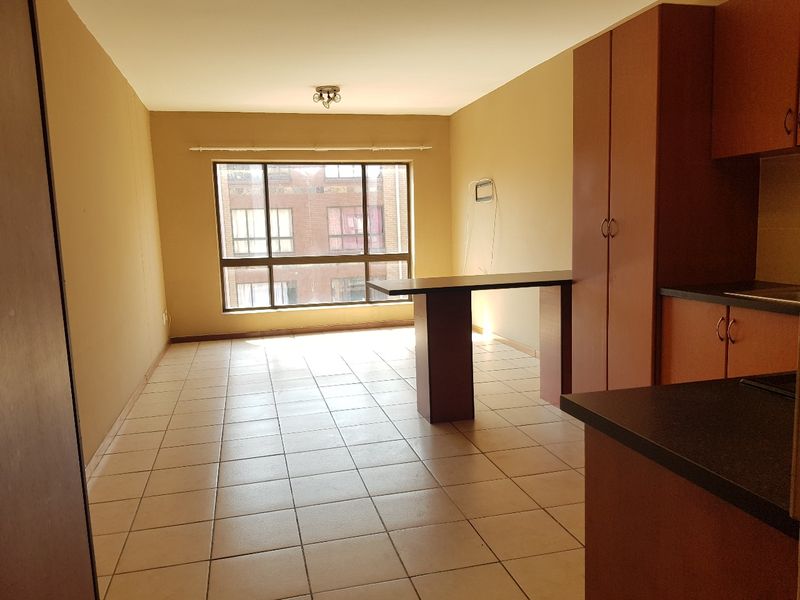 An open-plan living and kitchen area featuring tiled flooring, built-in cabinetry, and a breakfast bar, offering a functional and versatile living space.