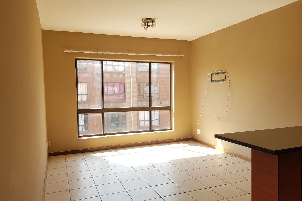 An empty open-plan living area featuring tiled flooring, a breakfast bar, and a large window providing natural light.