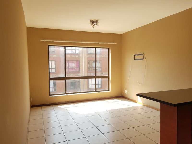 An empty open-plan living area featuring tiled flooring, a breakfast bar, and a large window providing natural light.