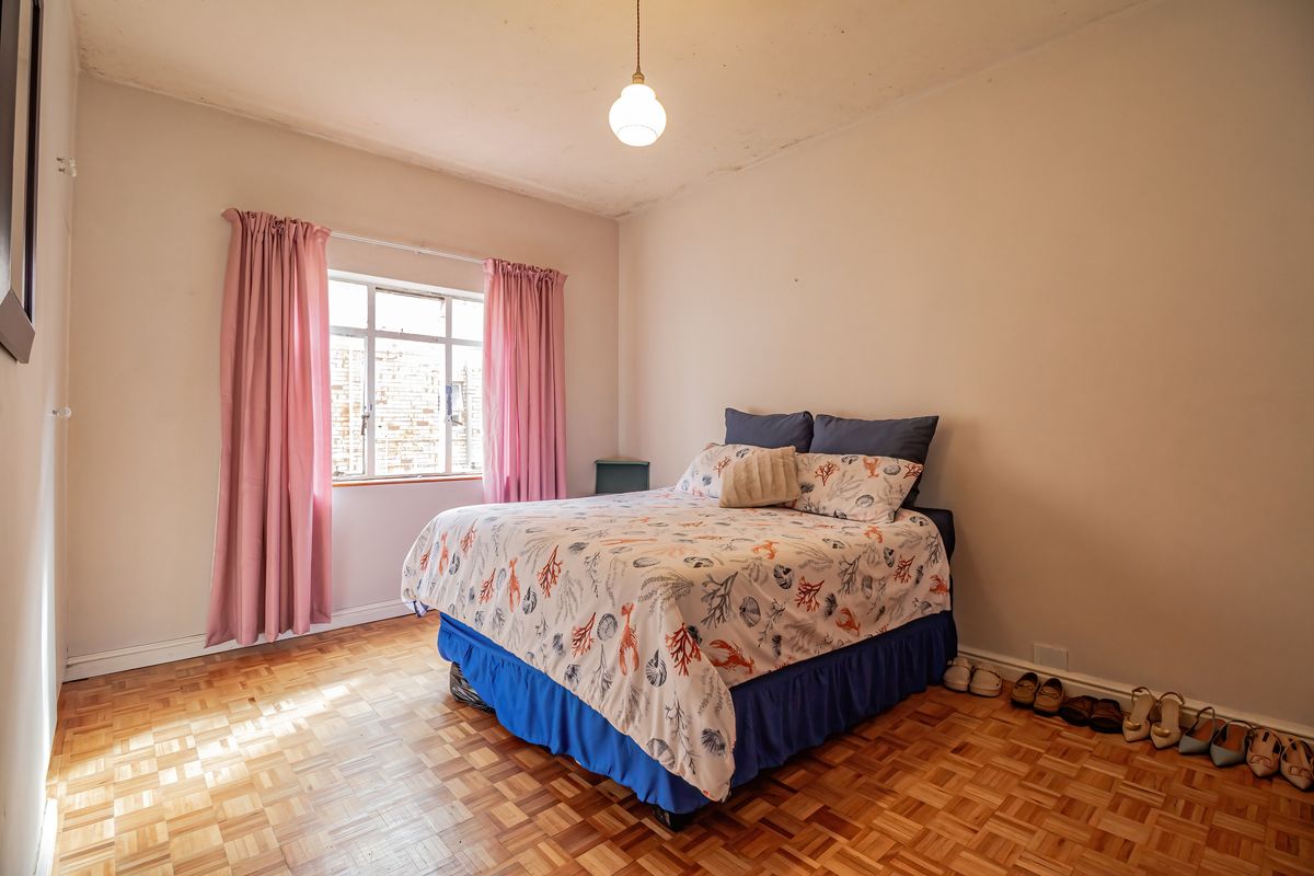 A bedroom featuring classic parquet flooring, a large casement window, and a simple pendant light fixture, offering a functional space with potential for updates.