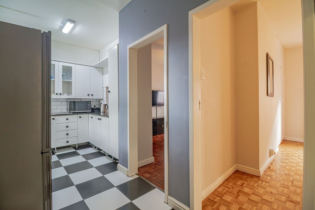 A functional kitchen featuring white cabinetry, subway tile backsplash, and checkerboard flooring, leading into a hallway with parquet wood flooring.