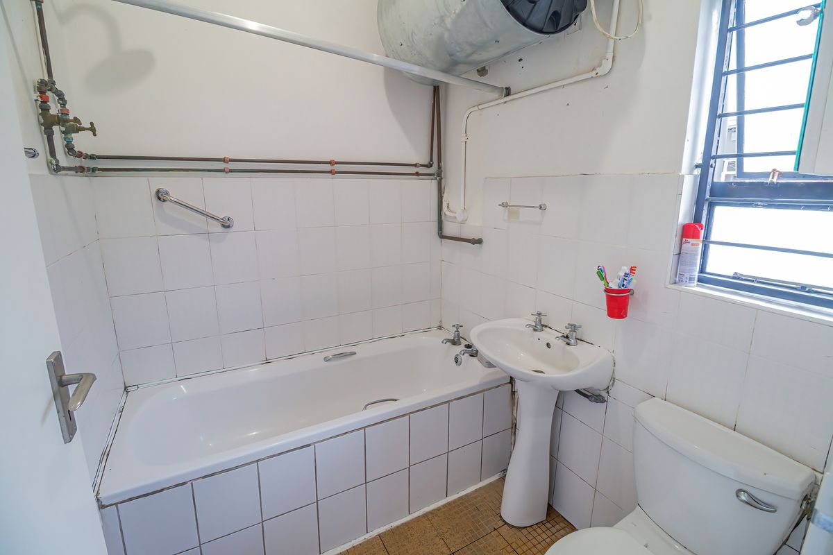 A functional bathroom featuring a bathtub, pedestal basin, and toilet, with exposed plumbing and dated tile finishes throughout.