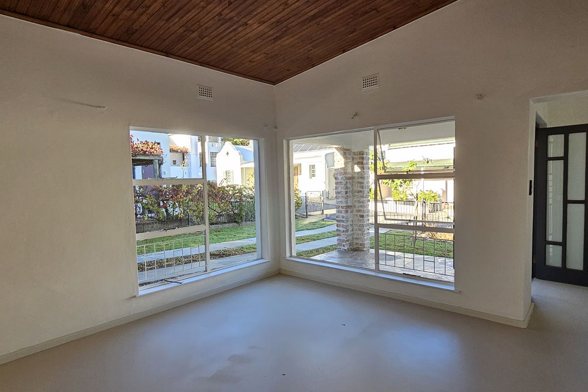 Bright and spacious living area featuring a warm timber ceiling, large windows providing natural light, and an exposed brick pillar detail.