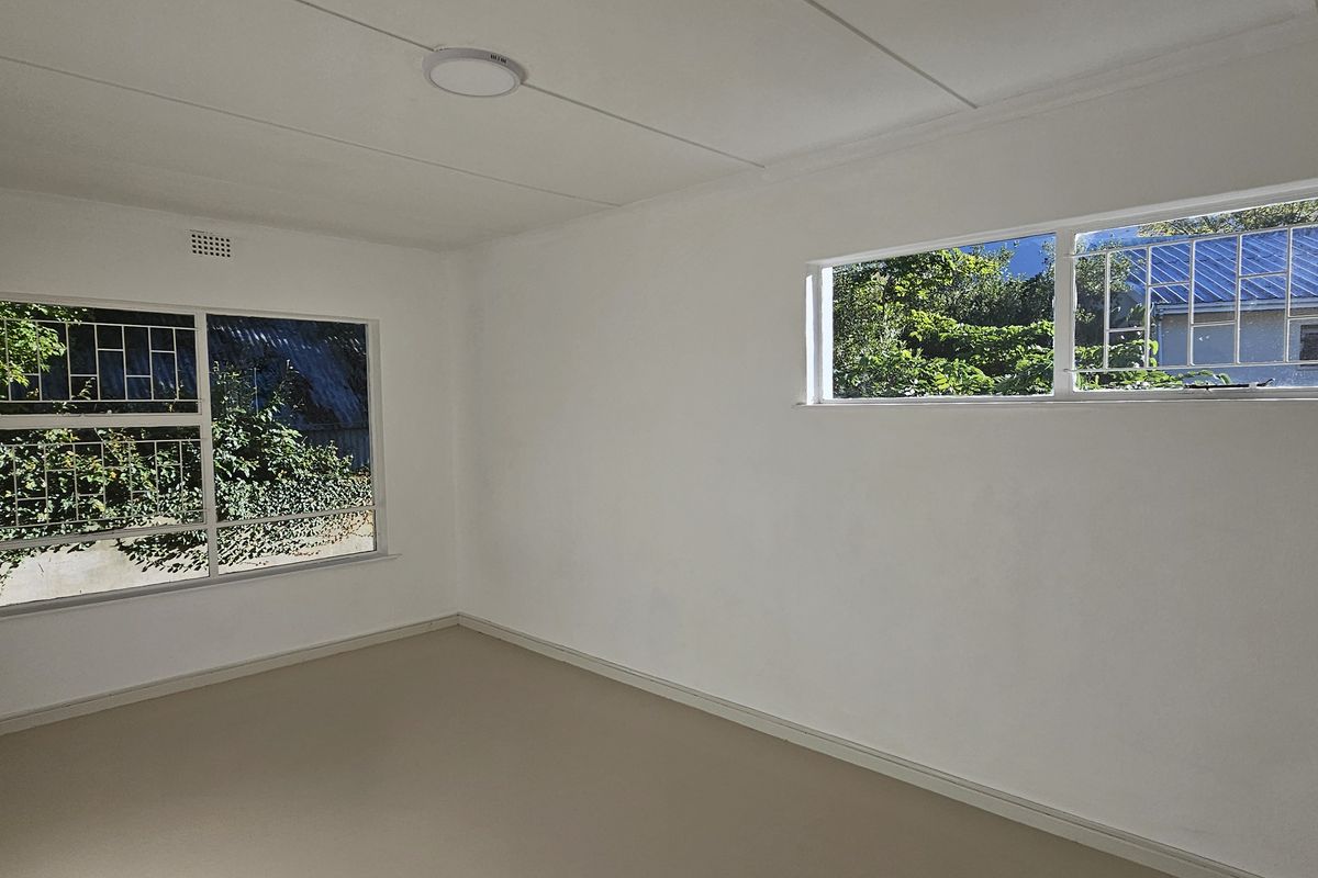 A vacant bedroom featuring neutral flooring, white walls, and windows fitted with security bars.