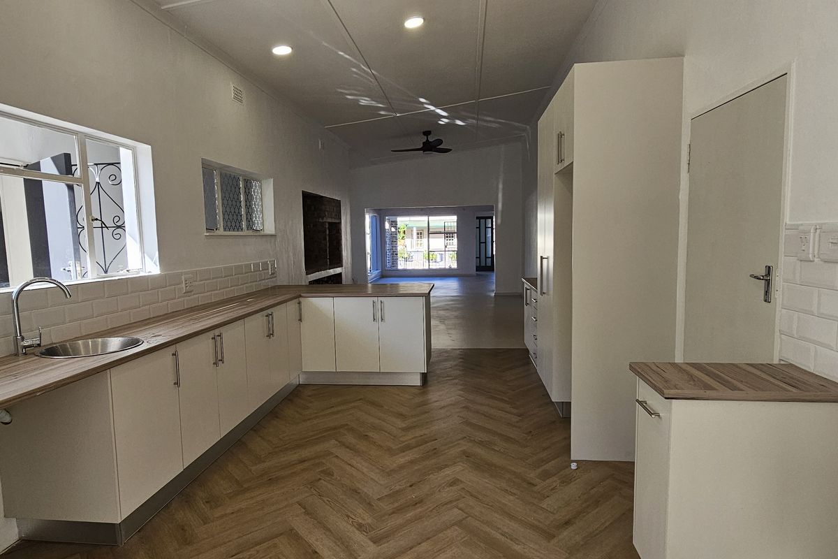 A bright, modern kitchen featuring white cabinetry, wood-look laminate countertops, subway tile backsplash, and herringbone flooring, leading into an open-plan living area.
