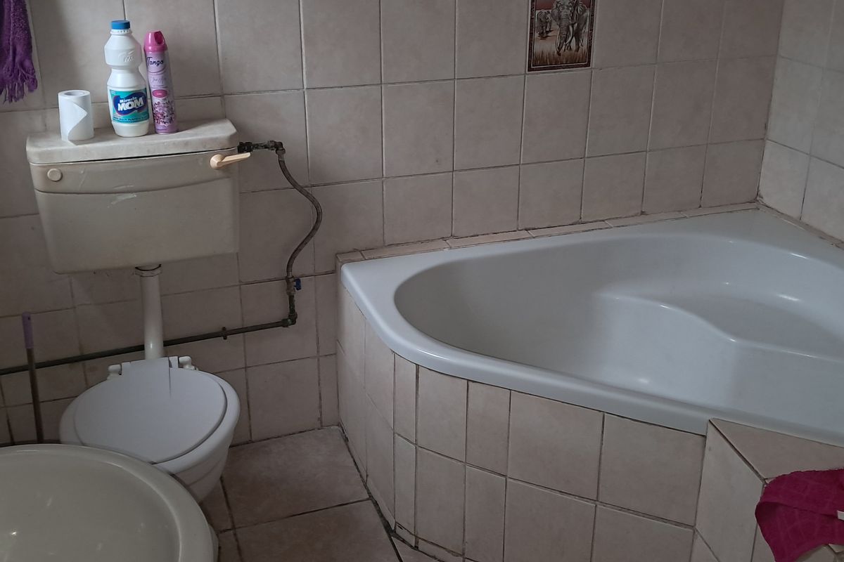 A compact bathroom featuring a corner bathtub, standard toilet, and washbasin with tiled walls and flooring.
