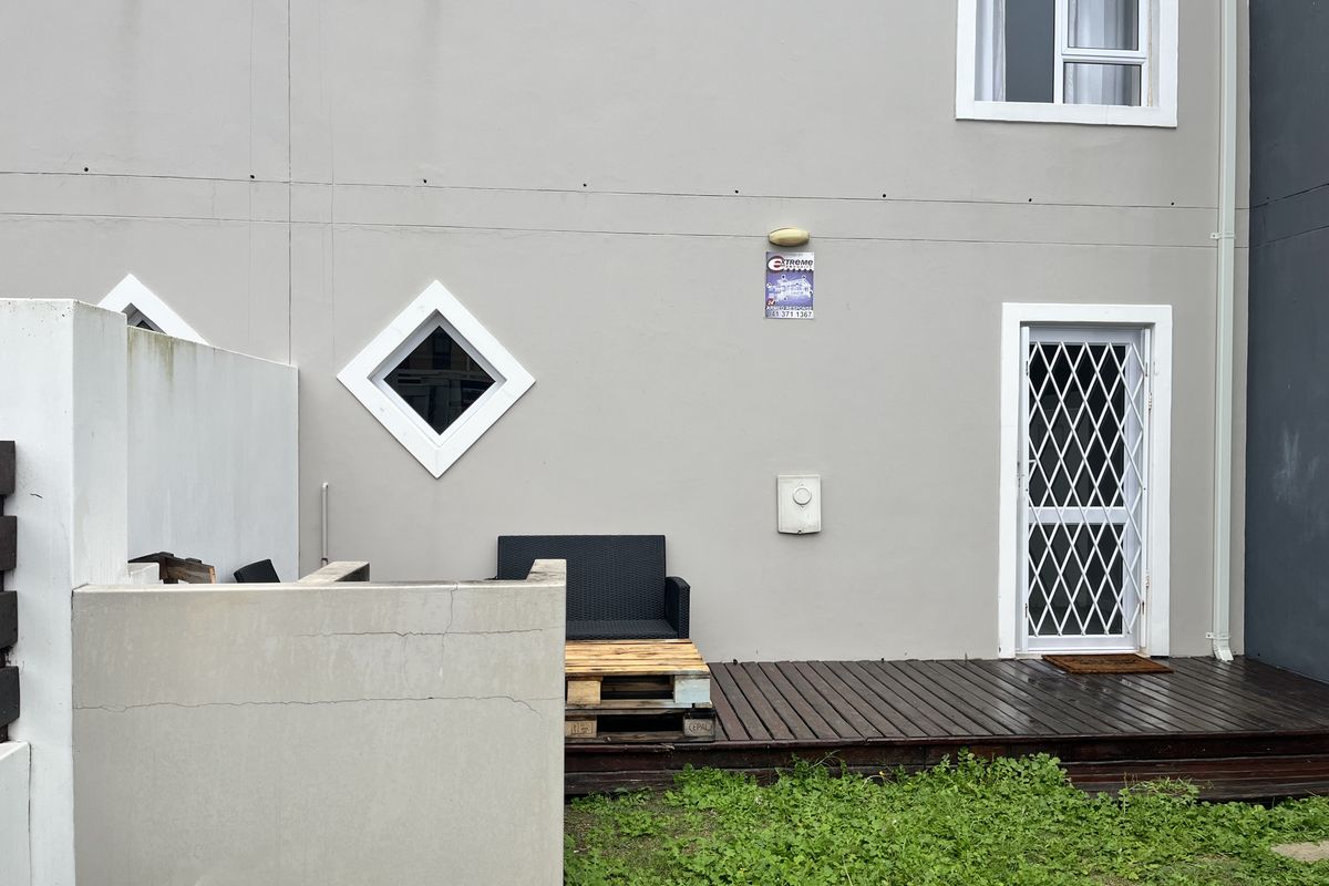 Rear exterior view featuring a timber deck, security gate, and masonry boundary wall with visible signs of weathering and minor structural cracking.
