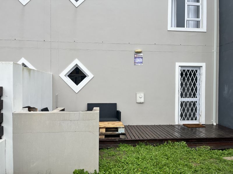 Rear exterior view featuring a timber deck, security gate, and masonry boundary wall with visible signs of weathering and minor structural cracking.