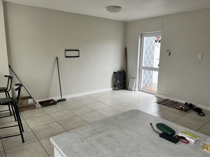 An open-plan living area featuring neutral tiled flooring, a security door, and a wall-mounted TV bracket, offering a blank canvas for interior design.