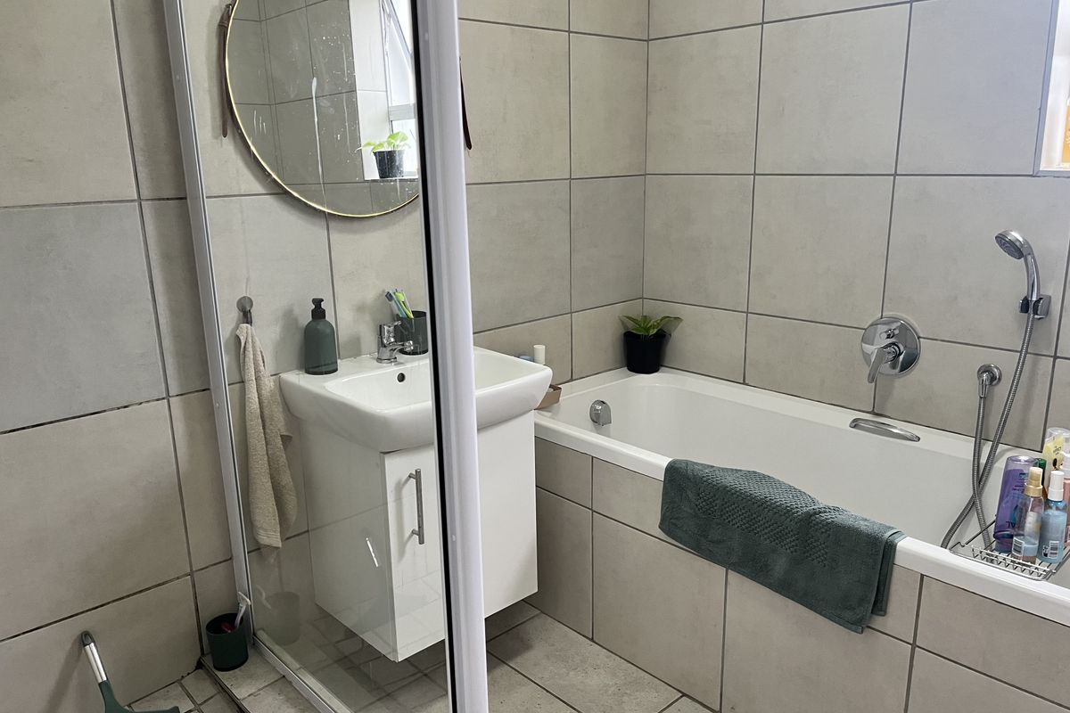 A functional bathroom featuring a vanity basin, bathtub with handheld shower attachment, and neutral wall and floor tiling.