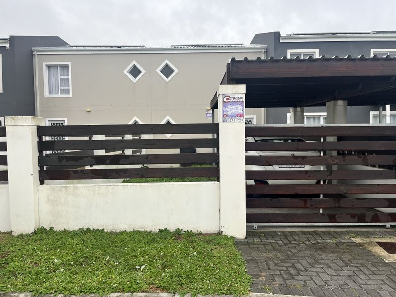 Front elevation of a townhouse featuring a timber slat fence, private carport, and distinctive diamond-shaped windows.