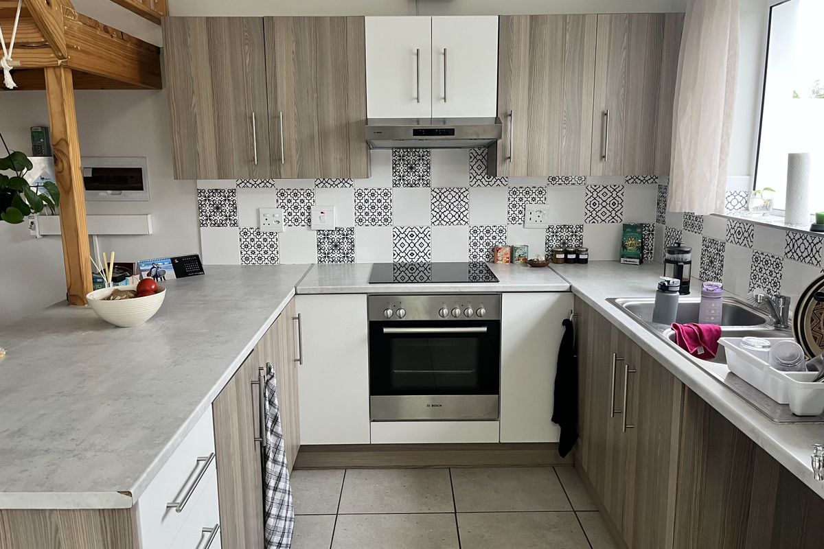 Modern U-shaped kitchen featuring wood-grain and white cabinetry, patterned tile backsplash, integrated electric hob, oven, and stainless steel sink.