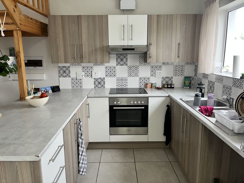 Modern U-shaped kitchen featuring wood-grain and white cabinetry, patterned tile backsplash, integrated electric hob, oven, and stainless steel sink.