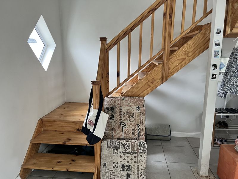 A hallway area featuring a timber staircase with a unique diamond-shaped window and neutral tiled flooring.