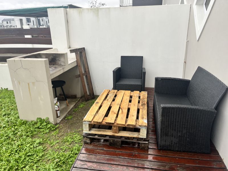 Outdoor patio area featuring a built-in braai, timber decking, and a boundary wall, offering a functional space for outdoor entertaining.