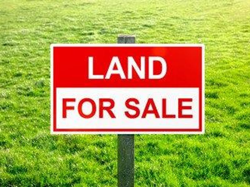 A vacant residential land plot featuring a prominent 'Land for Sale' sign set against a grassy field.