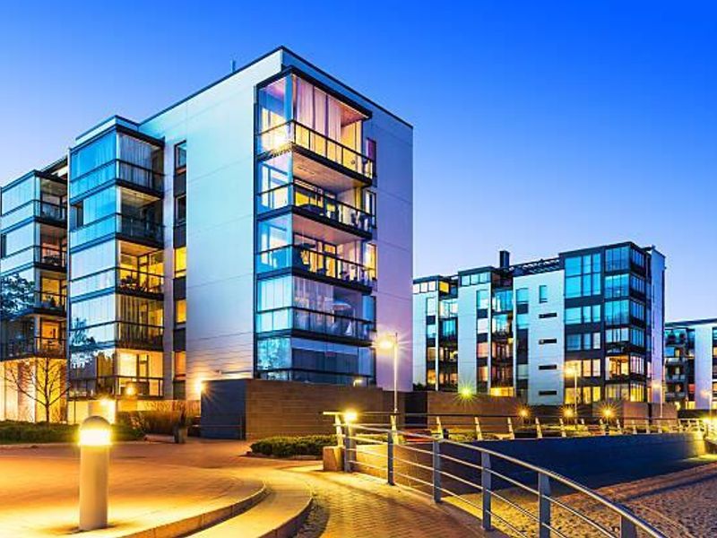 Modern multi-story residential apartment complex featuring glass-enclosed balconies and contemporary architectural design, captured during twilight with integrated exterior lighting.