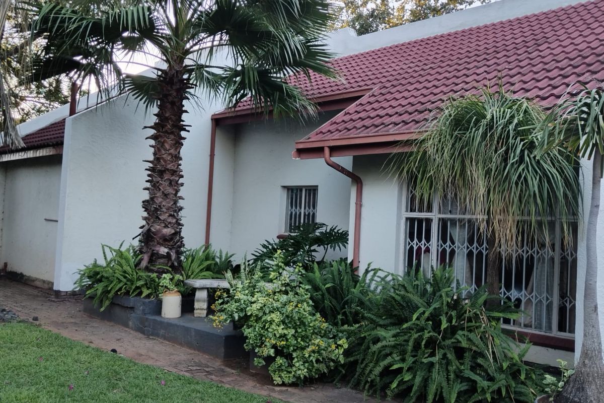 Rear exterior view of the house featuring a tiled roof, security bars on windows, and a landscaped garden area with a raised planter bed.