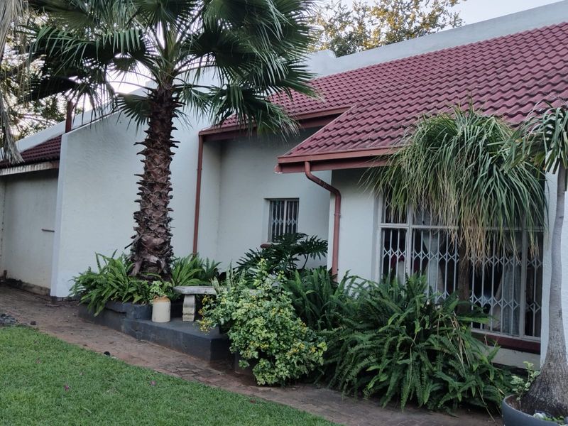 Rear exterior view of the house featuring a tiled roof, security bars on windows, and a landscaped garden area with a raised planter bed.