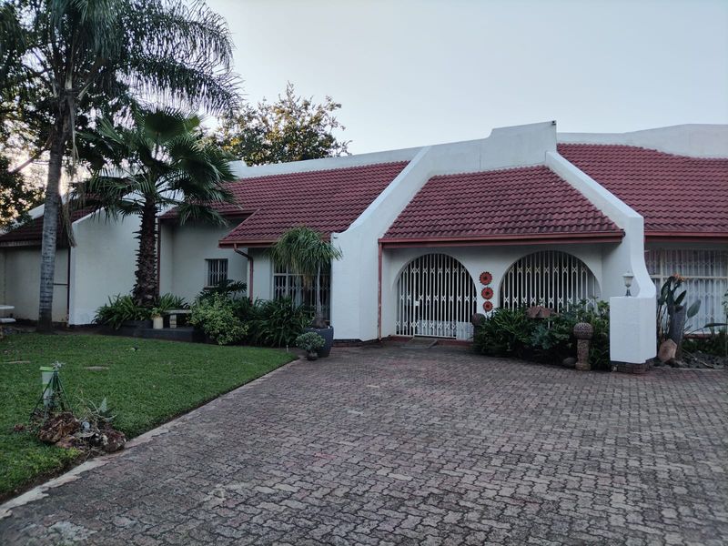 Front elevation of a residential property featuring a paved driveway, tiled roof, and secure arched entrance gates with established garden landscaping.