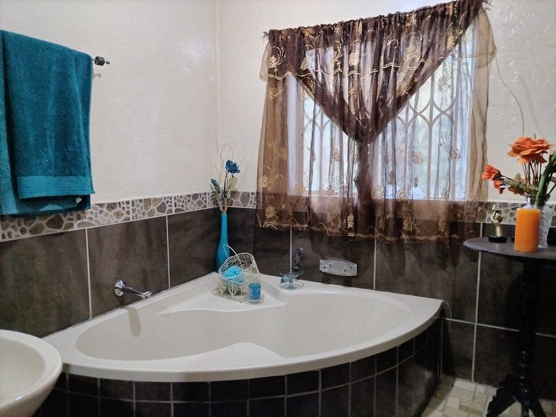 A bathroom featuring a corner bathtub with dark ceramic wall tiling and a window fitted with a security gate.