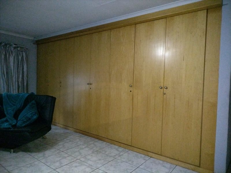A bedroom featuring extensive floor-to-ceiling built-in wooden cupboards and tiled flooring.