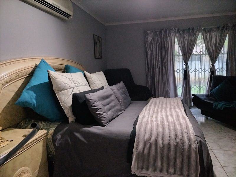 A bedroom featuring tiled flooring, a wall-mounted air conditioning unit, and a security gate over the window.