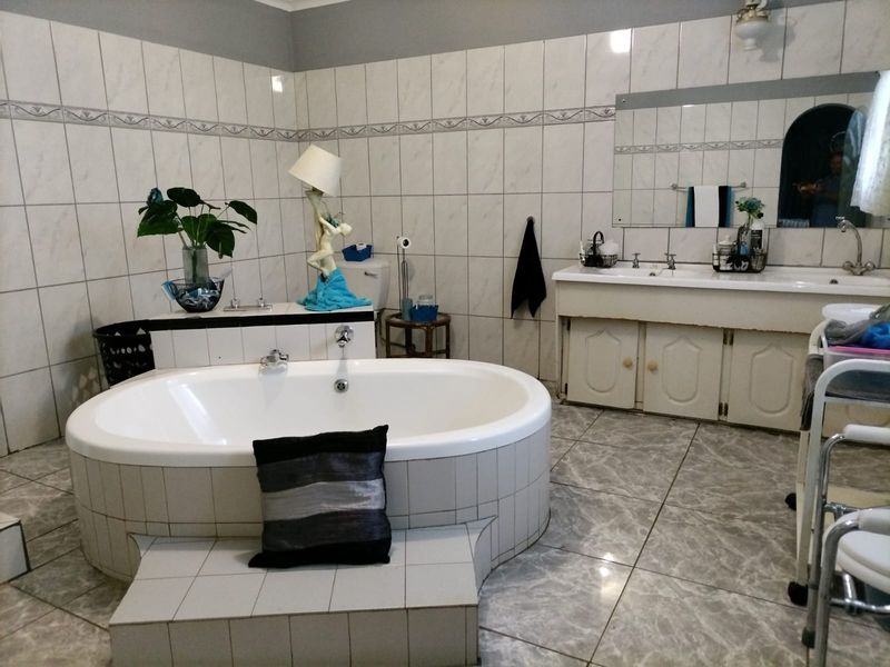Spacious bathroom featuring a built-in oval bathtub, double vanity with basin, and full-height wall tiling.