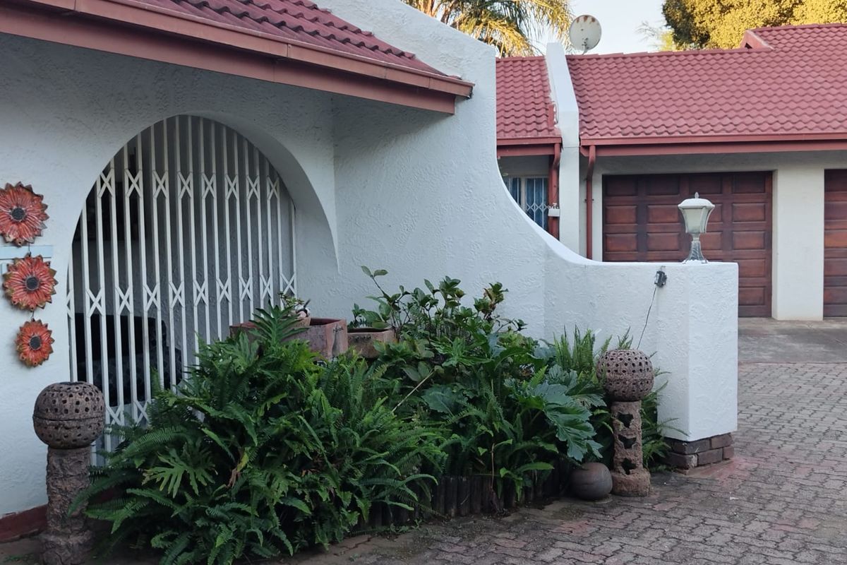 Front exterior view of the property featuring a paved driveway, garage access, and a covered entrance with a security gate.