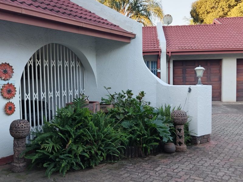 Front exterior view of the property featuring a paved driveway, garage access, and a covered entrance with a security gate.