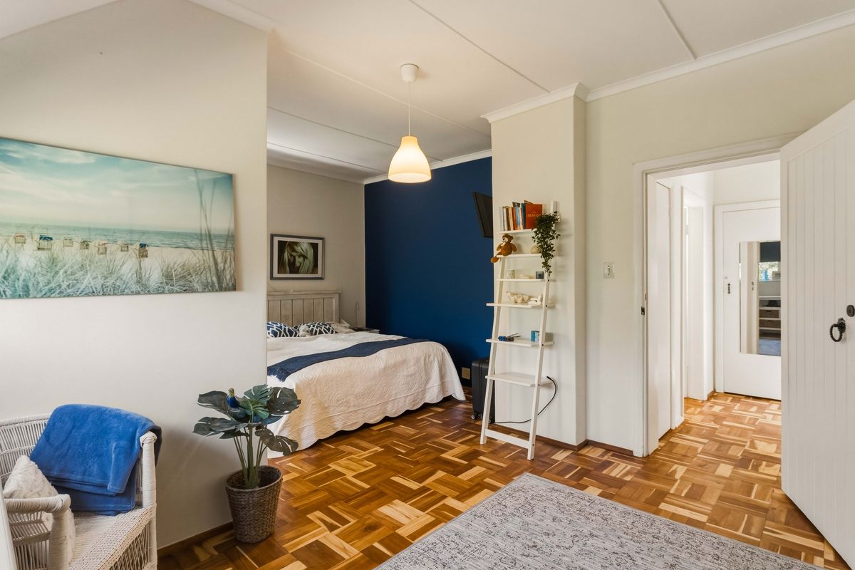 A well-lit bedroom featuring classic parquet flooring, a bold blue accent wall, and neutral tones, providing a comfortable and inviting sleeping space.