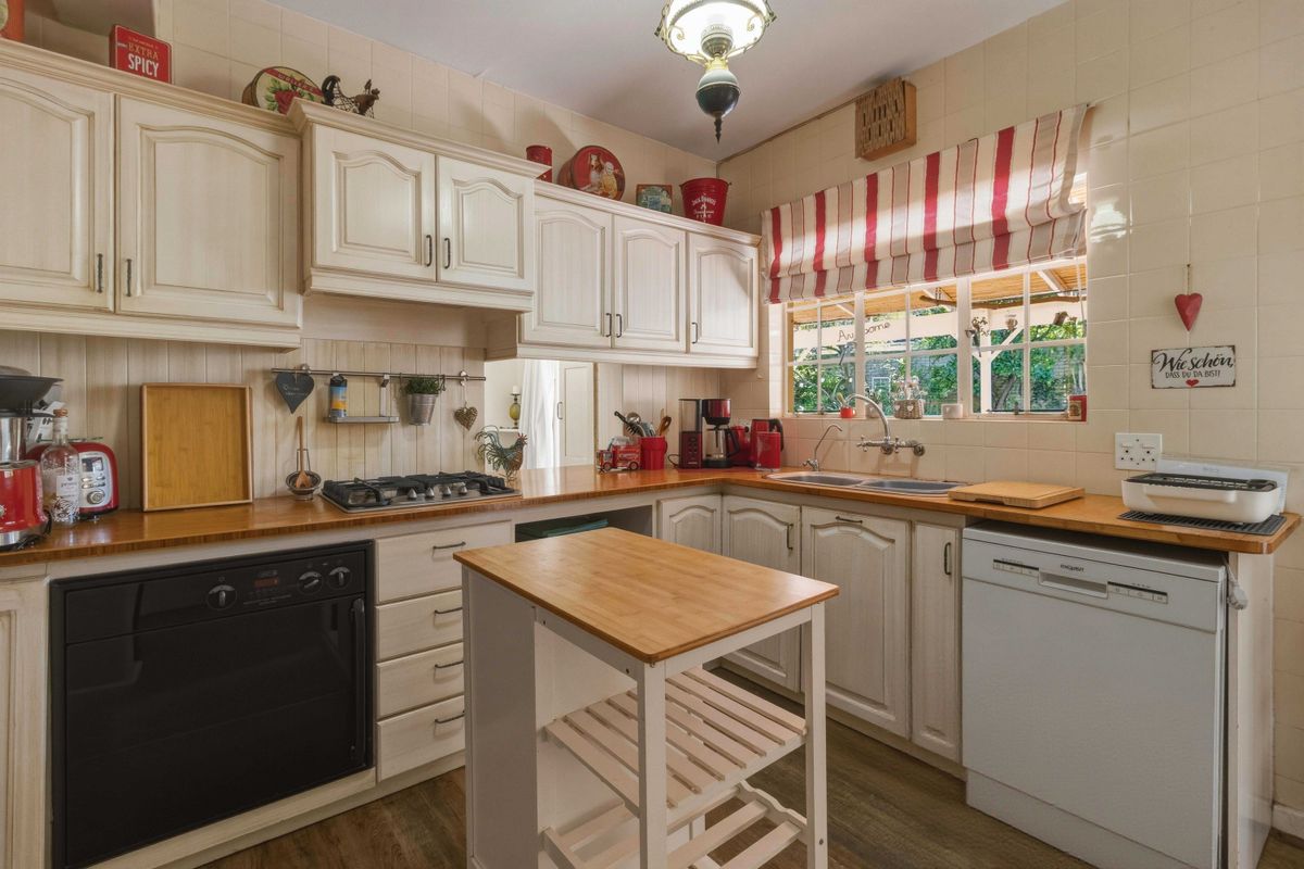 A functional kitchen featuring traditional cabinetry, wooden countertops, a gas hob, built-in oven, and a double sink with a tiled splashback.